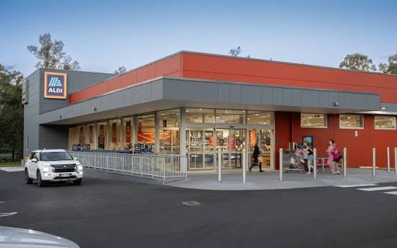 The ALDI Flagstone store at dusk, red and grey panelled walls and a glazed shopfront under a cantilevered awning