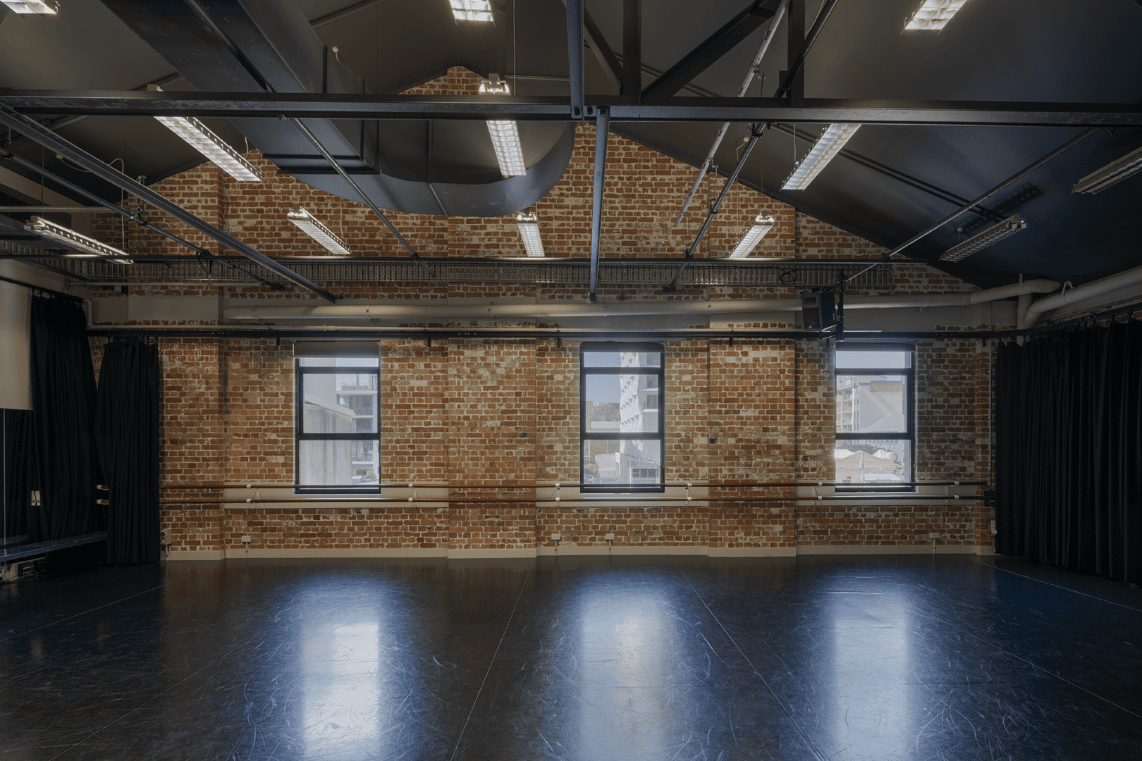 Interior rehearsal room at the Judith Wright Arts Centre, exposed brick walls and a black-painted timber roof structure with steel tie rods