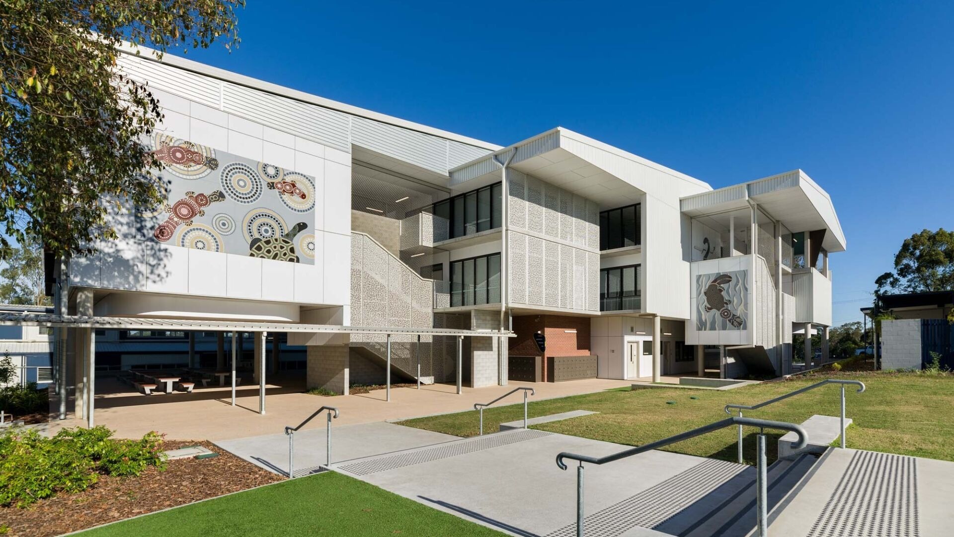 The Mabel Park STEM precinct building, white concrete blades and Aboriginal-art facade panels above a paved forecourt