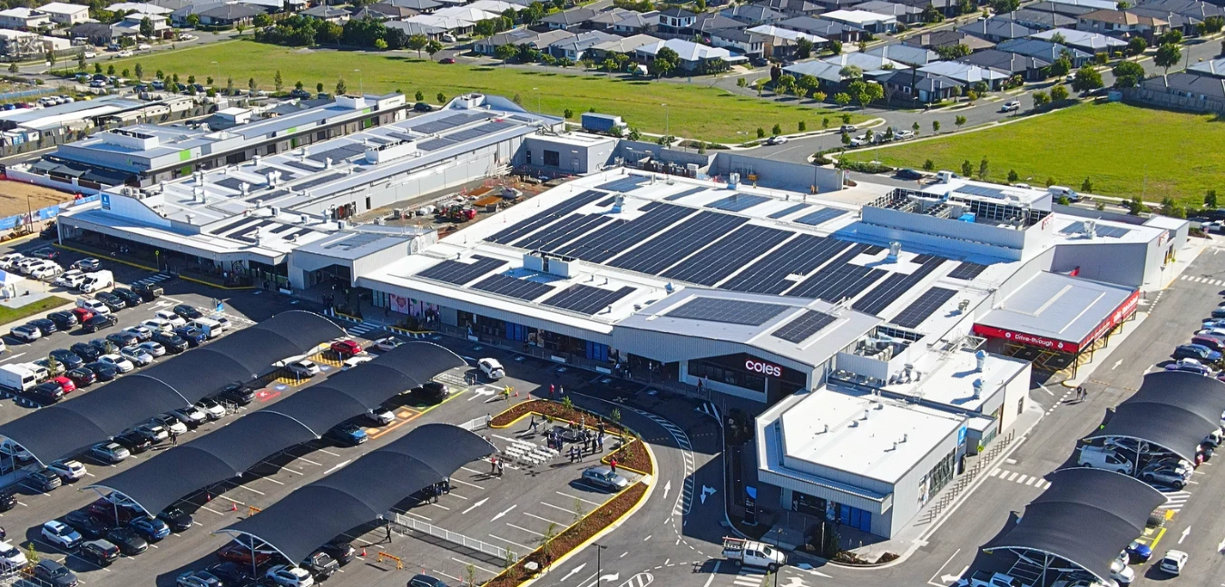 Aerial view of Providence Town Centre, a single-storey retail centre with extensive rooftop solar and shade-sail car parking beside a new housing estate