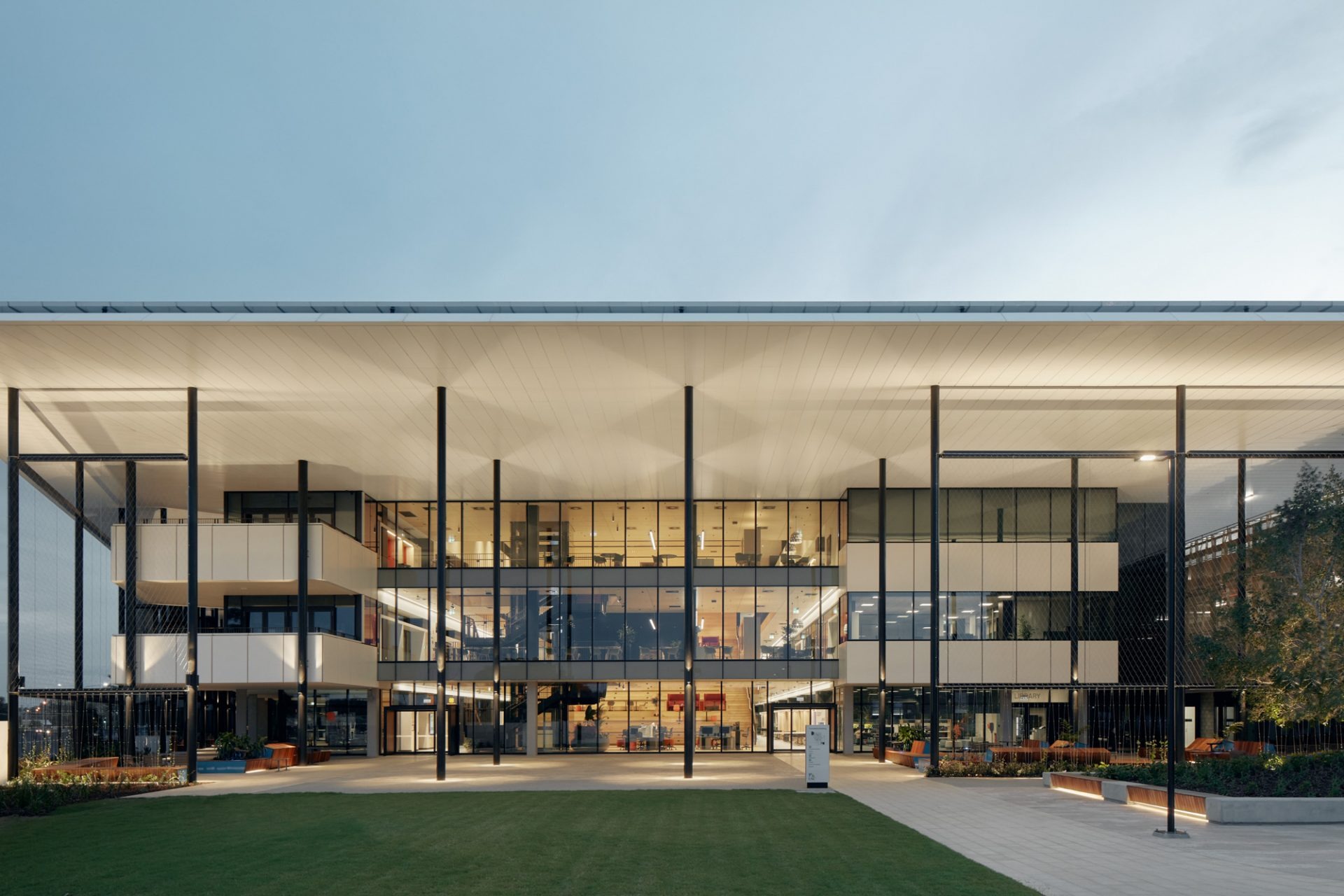 The UniSC Petrie foundation building at dusk, a deep flat roof canopy on slender columns over a glazed facade